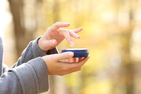 Close up of woman hand holding moisturizer cream bottle in fall in a parkの写真素材