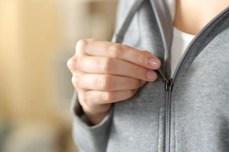 Close up of teen hand dressing closing zipper of gray hoodie at home