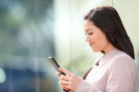 Side view of busineswoman reading text on smart phone standing in the streetの写真素材