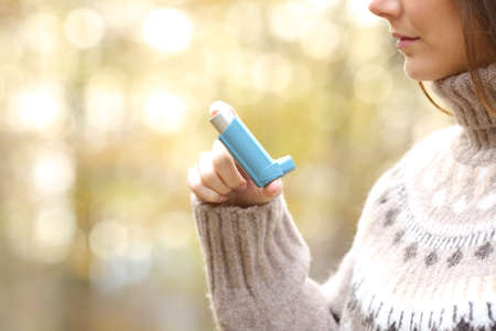 Close up profile of woman hand holding asthma inhaler ready to use in winter in a park