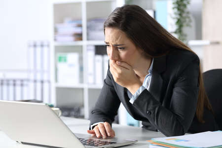Sad executive woman reading bad news on laptop sitting on a desk at the officeの写真素材
