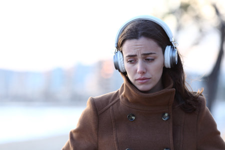 Front view of a sad woman walking alone wearing headphones listening to music in winter on the beachの写真素材