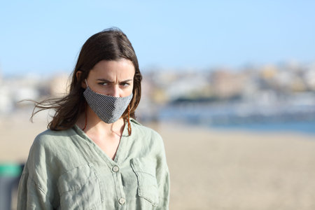 Angry woman walking wearing protective mask due covid on the beachの写真素材