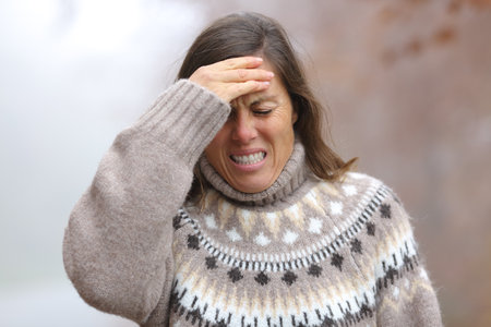 Adult woman suffering head ache walking in a park in a cold foggy winter dayの写真素材