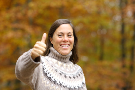 Happy adult woman gesturing thumbs up looking at camera in autumn in a parkの写真素材