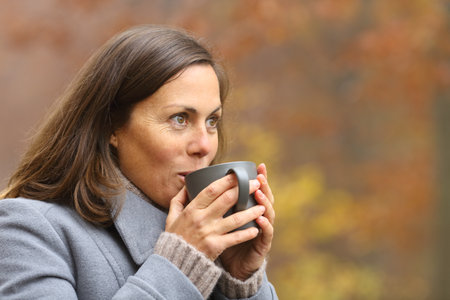 Adult woman drinking coffee standing in a park in autumn contemplating viewsの写真素材