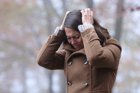 Desperate woman complaining alone grabbing hair with hands in a park in winterの写真素材