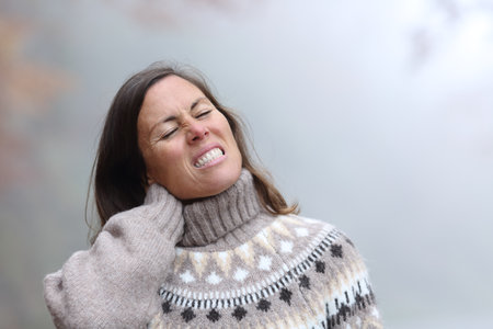 Middle age woman suffering neck ache in a cold and foggy winter dayの写真素材