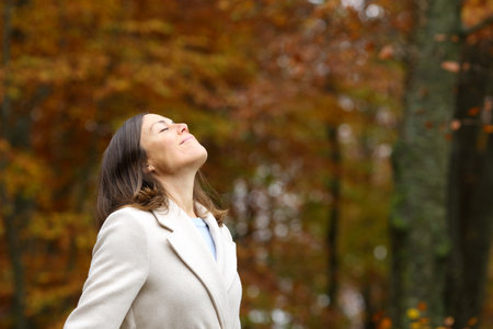 Adult woman breathing fresh air standing in a park in autumnの写真素材