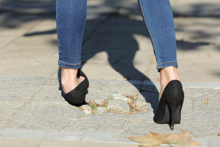Back view portrait of a woman legs walking spraining ankle stumbling with bump in the streetの写真素材