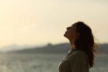 Profile of a back light of woman silhouette breathing deep fresh air on the beachの写真素材