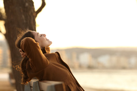 Profile of a woman resting sitting on a bench on the beach in winter at sunsetの写真素材