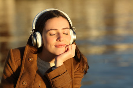 Happy woman listening to music wearing headphones relaxing at sunset in winter on the beachの写真素材