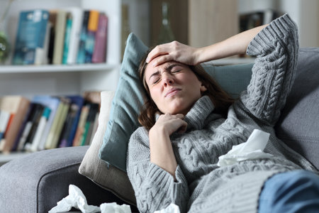 Ill woman suffering flu symptoms with headache lying on a couch at homeの写真素材
