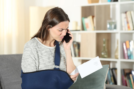 Sad disabled woman claiming on mobile phone about paper notice at homeの写真素材