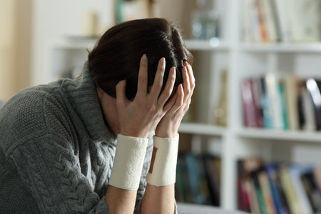 Sad woman complaining with bandages on wrists after suicide attempt at homeの写真素材