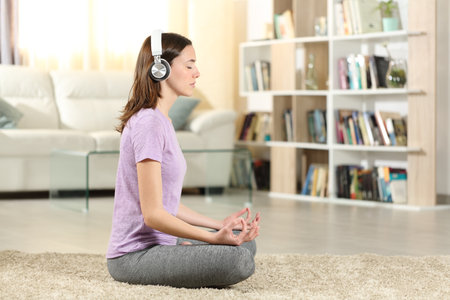 Side view portrait of a mindfulness woman doing yoga listening tutorial with headphones at homeの写真素材