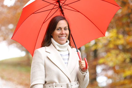 Happy woman posing looking at camera in winter with umbrella in a parkの写真素材