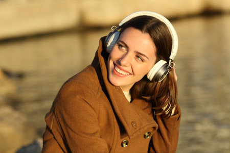 Happy woman wearing headphones listenng to music in winter in a parkの写真素材