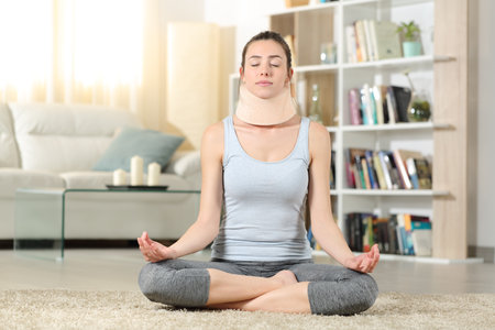 Front view portrait of a disabled woman with neck brace doing yoga exercise at homeの写真素材