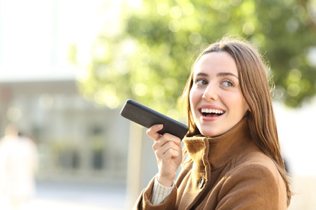 Portrait of a happy woman dictating message on smart phone in winter in the streetの写真素材