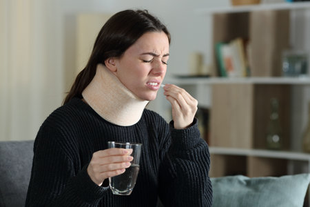 Disabled woman with ache taking pill complaining sitting on a couch at homeの写真素材