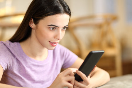 Concentrated woman checking content on smart phone sitting at homeの写真素材