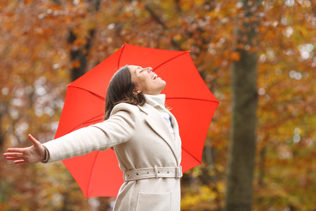 Happy middle aged woman breathing fresh air in winter with umbrella in a parkの写真素材