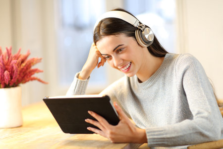 Happy woman wiearing headphones watching tablet content at homeの写真素材