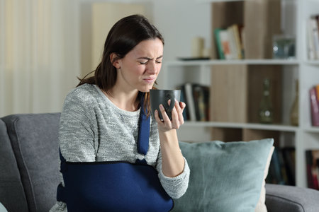 Disabled woman complaining drinking hot coffee sitting on a couch at homeの写真素材