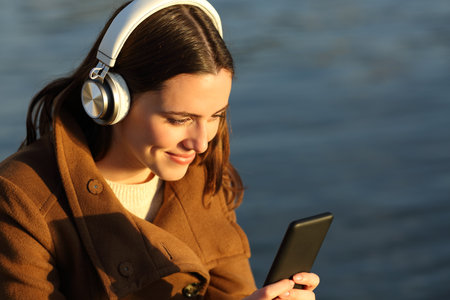 Happy female listening to music with smart phone and headphones on the beach in winterの写真素材