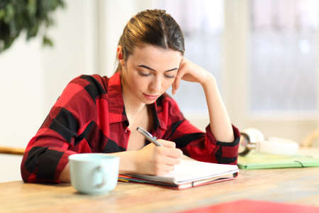 Concentrated student studying taking notes in the living room at homeの写真素材