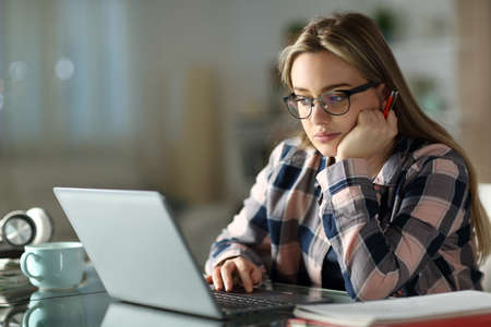Concentrated student wearing eyeglasses e-learning using laptop at home in the night