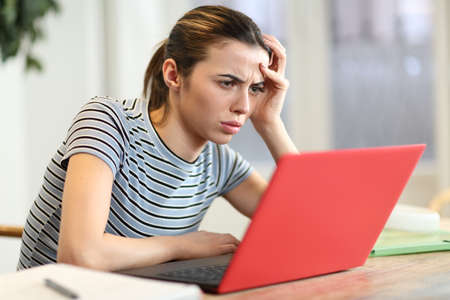 Worried woman checking red laptop in the living room at homeの写真素材
