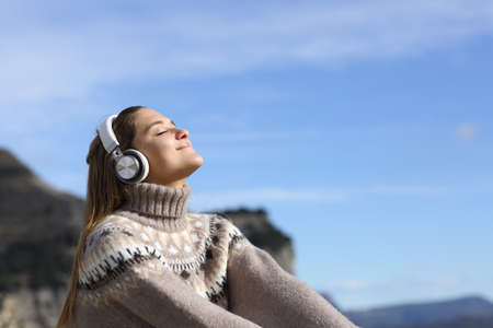 Happy woman relaxing listening to music with wireless headphones in the mountain in winterの写真素材