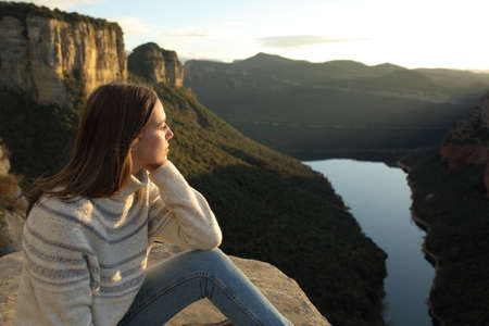 Pensive woman contemplating views in the top of a cliff in the mountain at sunset in winterの写真素材