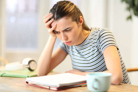 Frustrated student studying complicated lesson reading notes on notebook at homeの写真素材