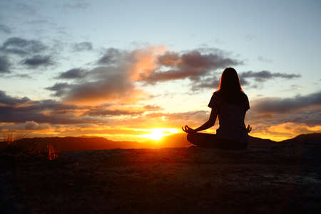 Back view portrait of a woman silhouette doing yoga at sunset in the mountainの写真素材