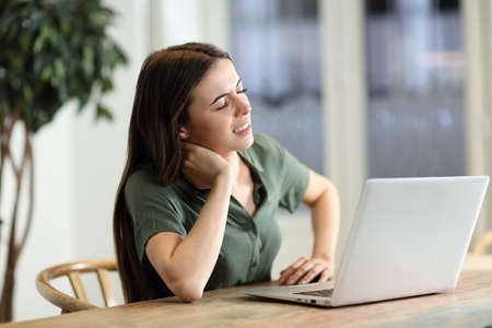 Stressed woman using laptop complaining having neck ache at homeの写真素材