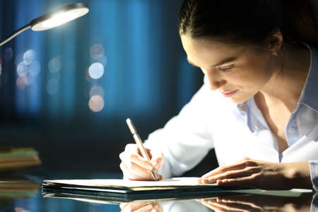 Woman filling paper form late hours in the night at officeの写真素材
