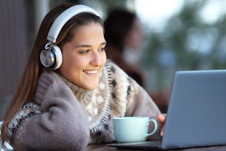 Happy woman wearing headphones watching and listening media on laptop sitting in a barの写真素材