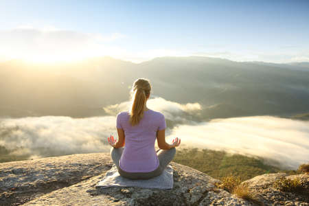 Back view of a woman in the top of a cliff meditating doing yogaの写真素材