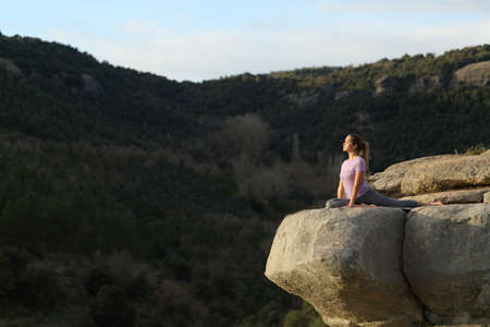 Concentrated yogi practicing yoga exercise in the top of a cliff in the mountainの写真素材