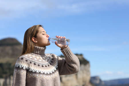 Side view portrait of a woman drinking water from plastic bottle in winter in the mountainの写真素材
