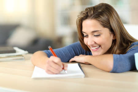 Happy woman taking notes on notebook in a table at homeの写真素材