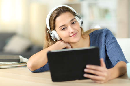 Satisfied woman watching media on tablet wearing headphones at homeの写真素材