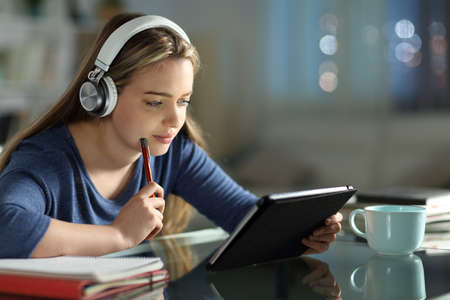 Student e-learning with tablet and headphones in the night in the living room at home