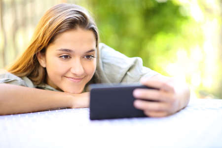 Satisfied woman watching videos on smart phone sitting in a garden at homeの写真素材