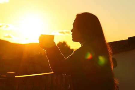 Backlight silhouette of a tenant drinking coffee contemplating sunset from a balconyの写真素材