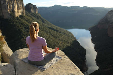 Back view portrait of a woman exercising yoga meditating in the mountainの写真素材